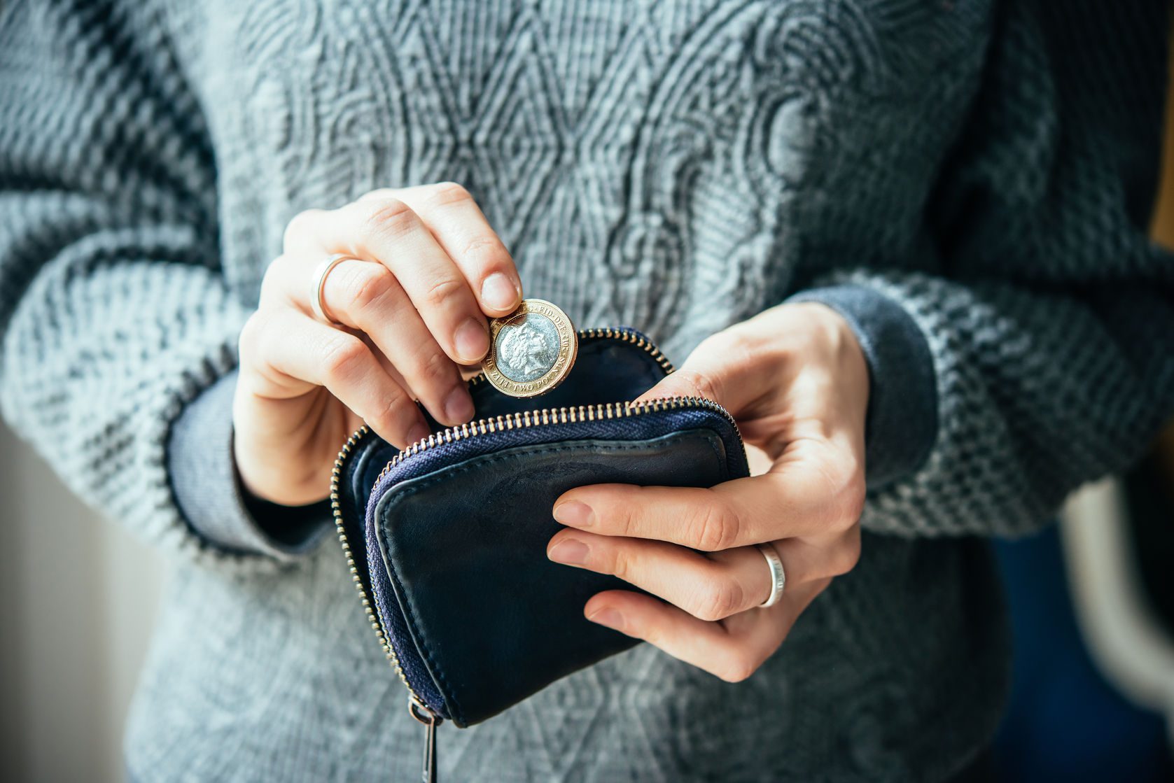 Hands-holding-british-pound-coin-and-small-money-pouch