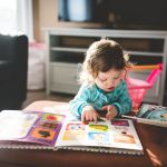 Photo of a young child reading a picture book that's on a coffee table in a sunlight living room